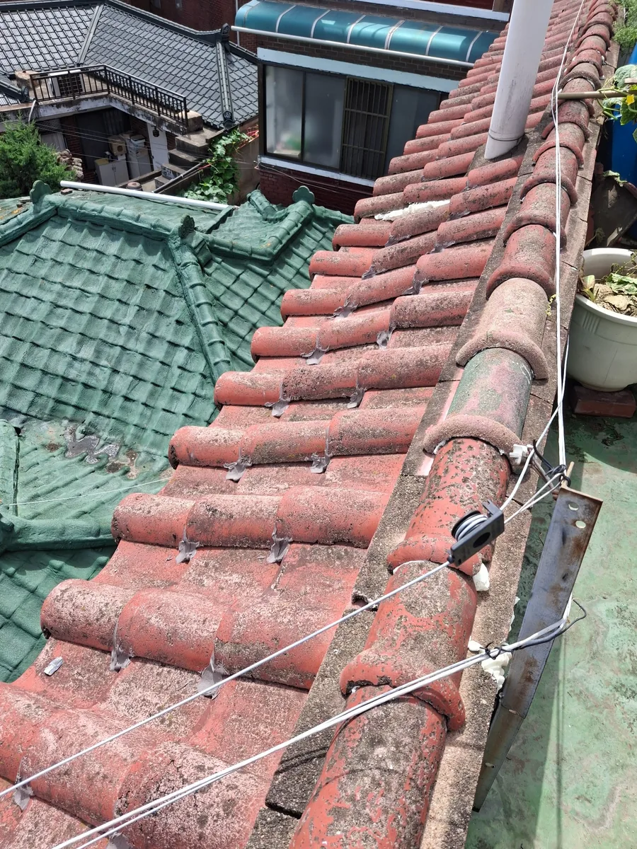 기와지붕부분수리 시공 후 붉은 기와 지붕의 부분 보수와 고정 상태 확인 사진